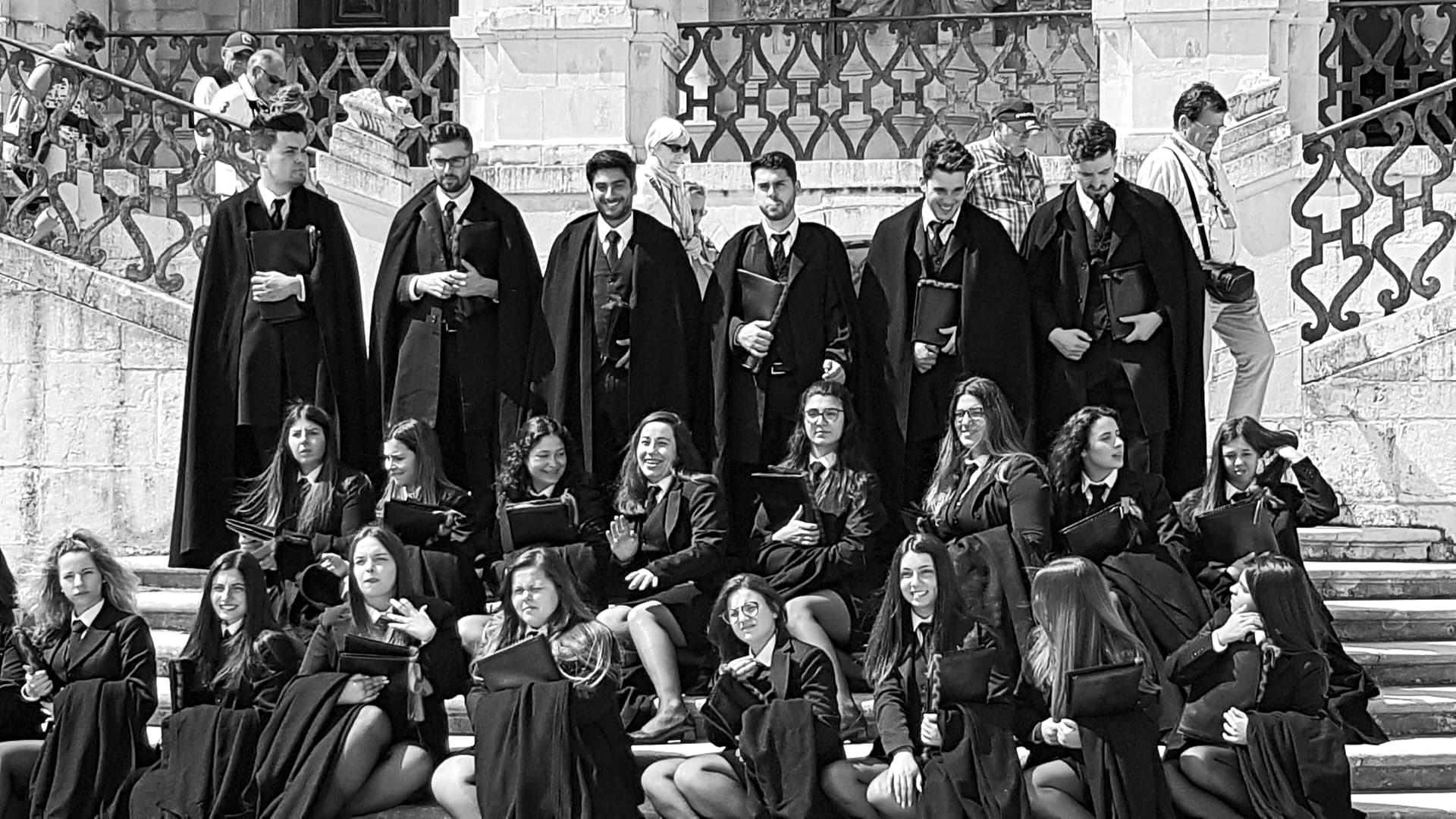 Estudantes de Coimbra de traje académico, sentados e de pé numa escadaria.